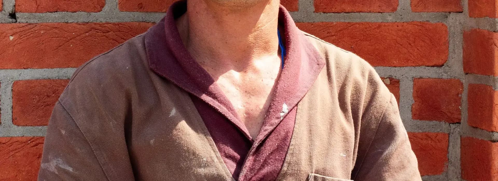Tradesman in work clothes standing in front of a brick wall