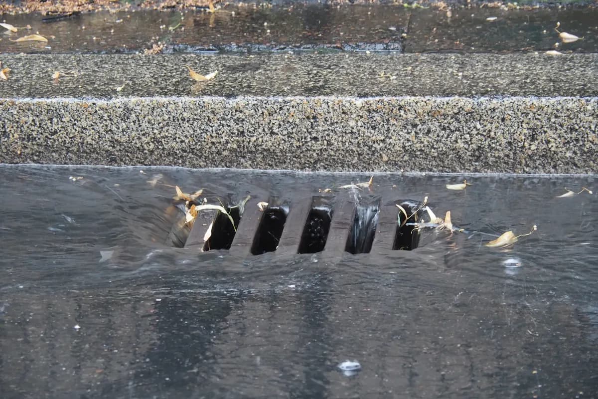 Heavy rain running across a road surface into a drain grate