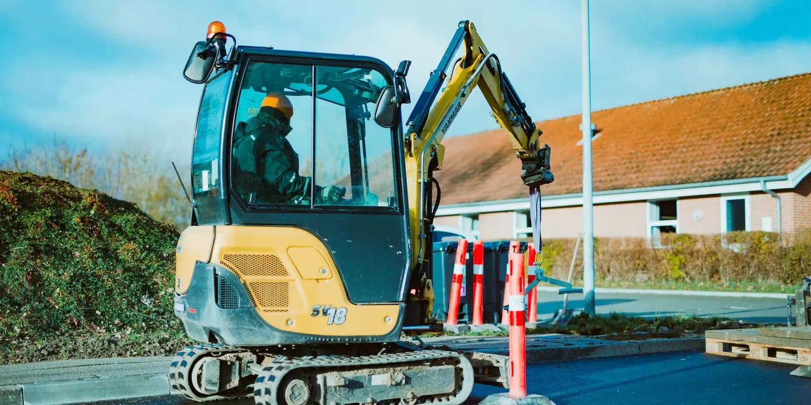 Operator in a hard hat using a compact mini digger beside a row of houses